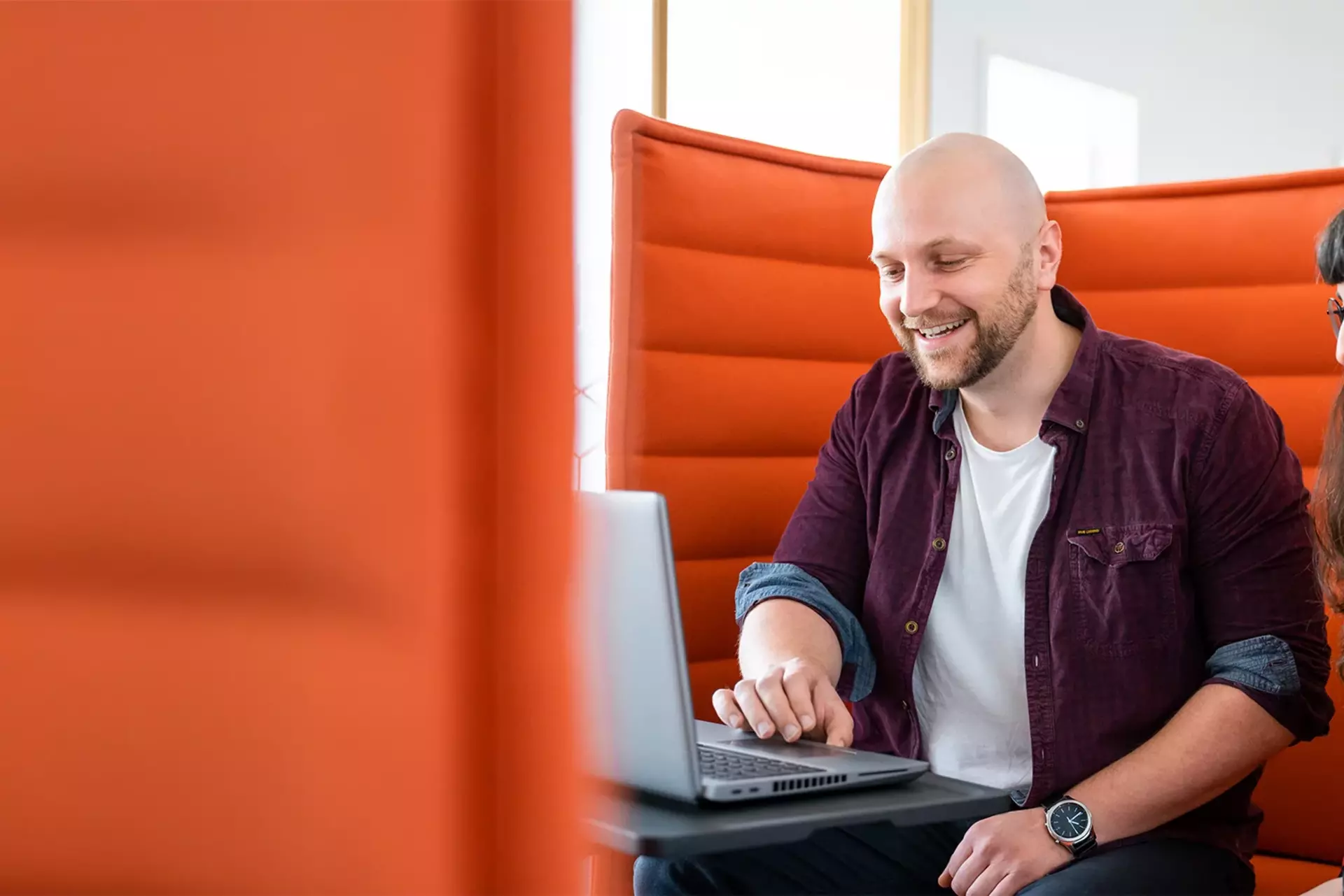 Zwei Mitglieder des Babtec-Teams arbeiten gemeinsam an einem Laptop auf einer orangefarbenen Couch.