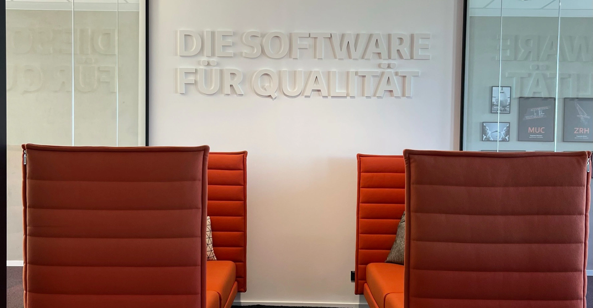 Zwei orangefarbene Sofas mit hoher Lehne, darüber ein Schriftzug "Die Software für Qualität"