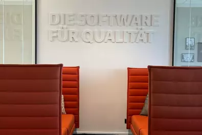 Zwei orangefarbene Sofas mit hoher Lehne, darüber ein Schriftzug "Die Software für Qualität"